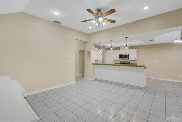 kitchen with kitchen peninsula, ceiling fan with notable chandelier, light tile patterned floors, white cabinetry, and hanging light fixtures