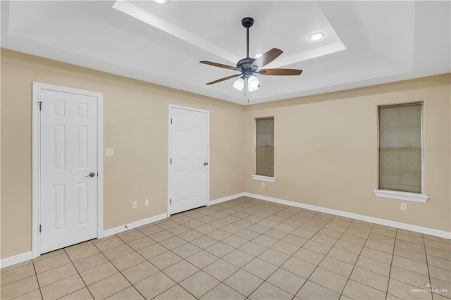 empty room with ceiling fan, light tile patterned floors, and a tray ceiling