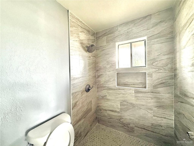 full bathroom with a tile shower and toilet