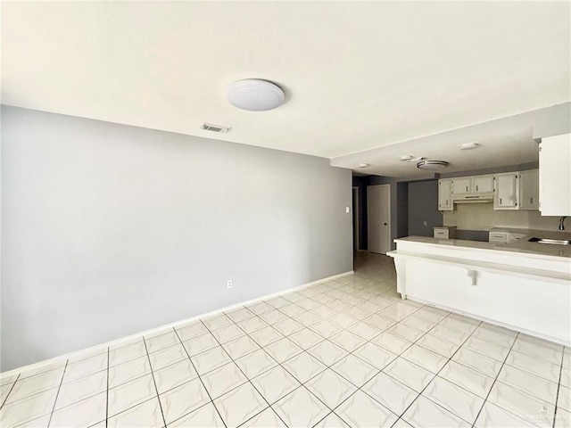 kitchen featuring baseboards, visible vents, a peninsula, light countertops, and a sink