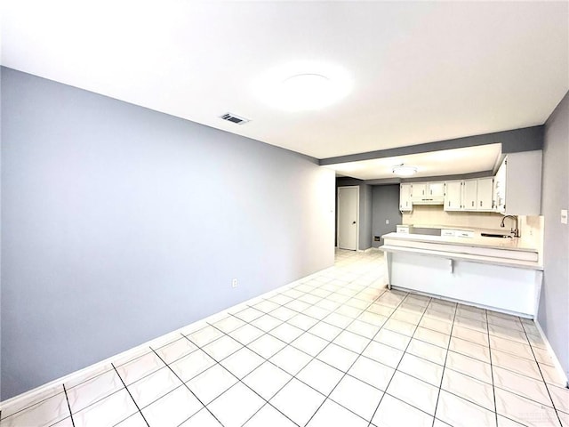 kitchen with visible vents, a kitchen breakfast bar, a peninsula, light countertops, and a sink