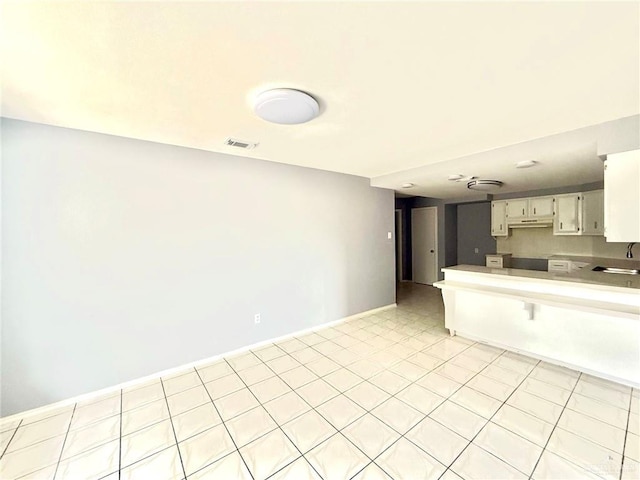 kitchen with a peninsula, a sink, visible vents, white cabinets, and baseboards