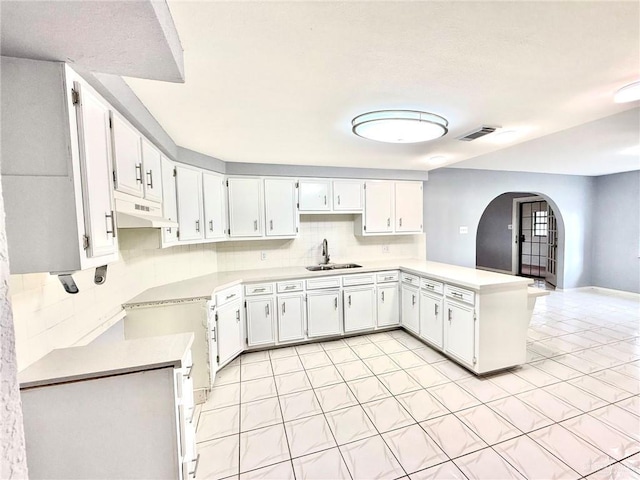 kitchen with arched walkways, under cabinet range hood, a peninsula, a sink, and visible vents