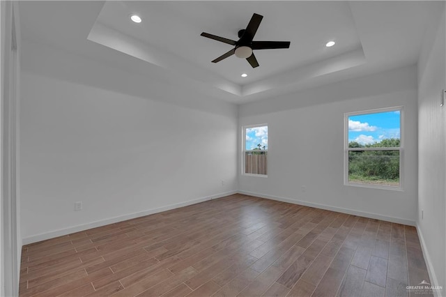 spare room with ceiling fan, light hardwood / wood-style floors, and a raised ceiling