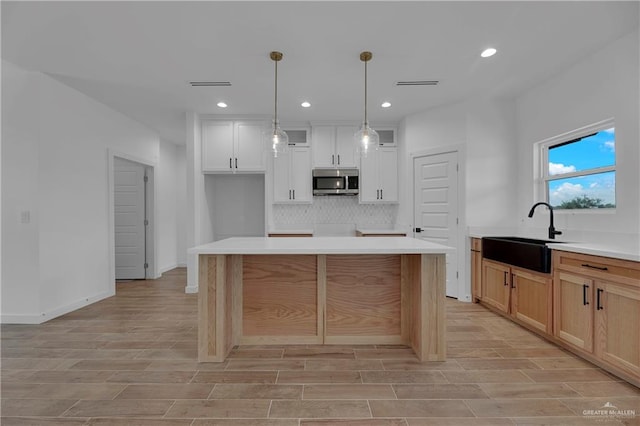 kitchen featuring light wood-type flooring, a kitchen island, sink, pendant lighting, and white cabinetry