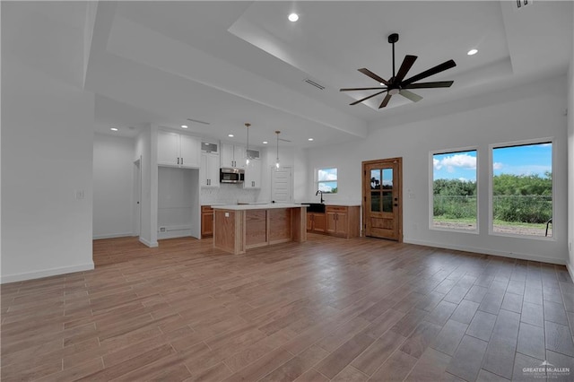 unfurnished living room with ceiling fan, a raised ceiling, light wood-type flooring, and sink