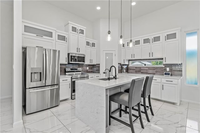 kitchen with sink, an island with sink, appliances with stainless steel finishes, decorative light fixtures, and white cabinetry