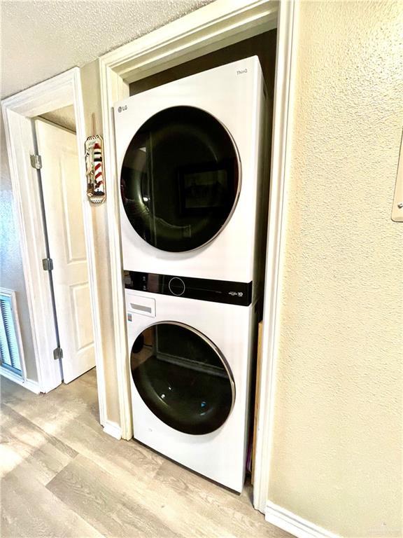 laundry room featuring stacked washer and clothes dryer and light hardwood / wood-style flooring