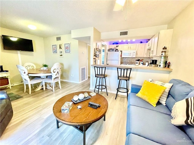 living room with light wood-type flooring, visible vents, a textured ceiling, and baseboards