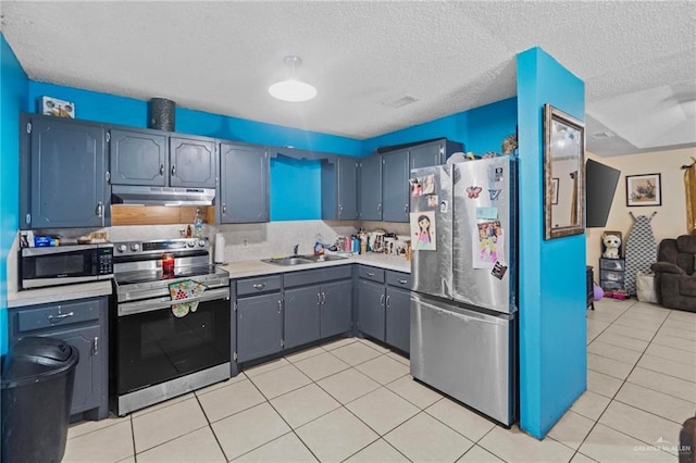 kitchen with sink, backsplash, light tile patterned floors, stainless steel appliances, and a textured ceiling