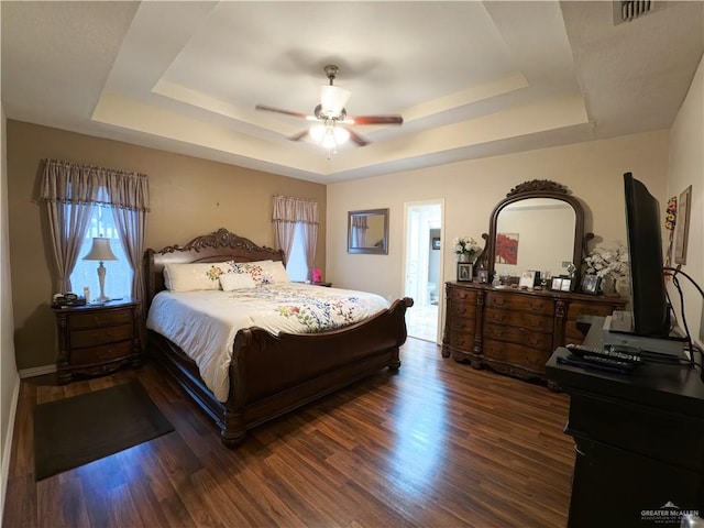 bedroom featuring a raised ceiling, ceiling fan, ensuite bathroom, and dark wood-type flooring