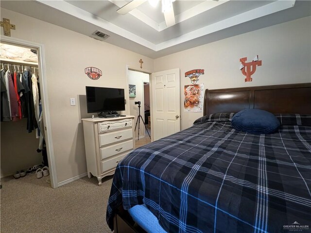 bedroom with light colored carpet, a tray ceiling, ceiling fan, a spacious closet, and a closet