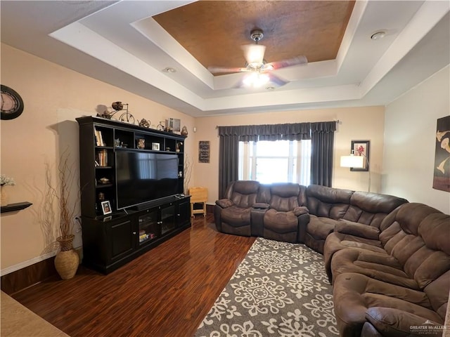 living room featuring dark hardwood / wood-style flooring, a tray ceiling, and ceiling fan