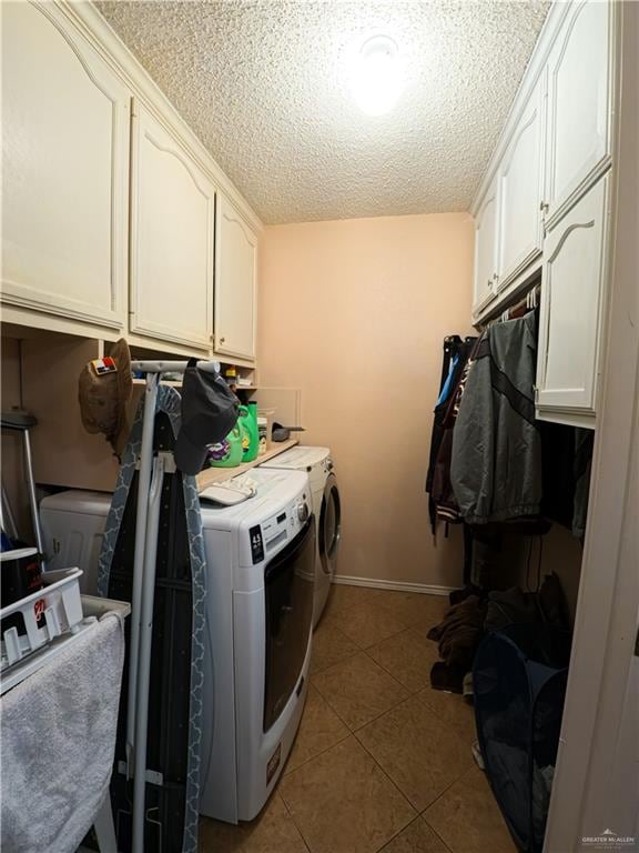 clothes washing area with cabinets, light tile patterned floors, a textured ceiling, and washing machine and clothes dryer