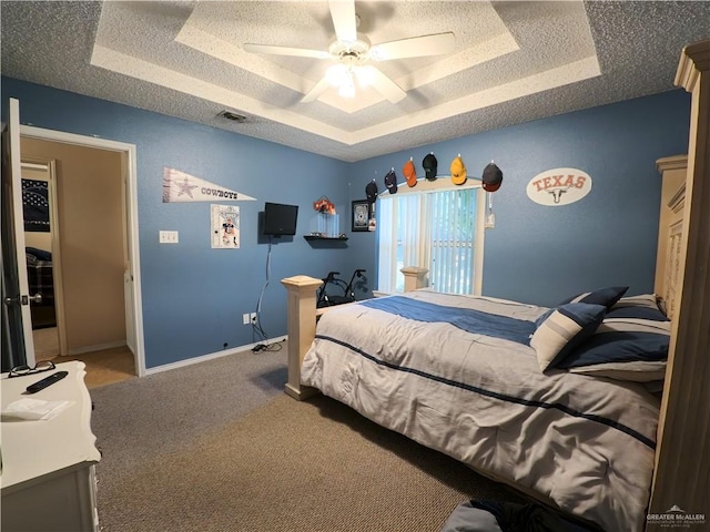 carpeted bedroom featuring a tray ceiling, ceiling fan, and a textured ceiling