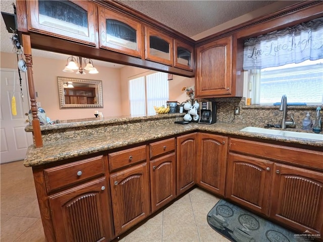 kitchen featuring sink, an inviting chandelier, stone countertops, a textured ceiling, and light tile patterned floors