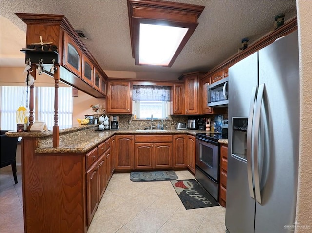 kitchen with kitchen peninsula, appliances with stainless steel finishes, backsplash, sink, and stone counters