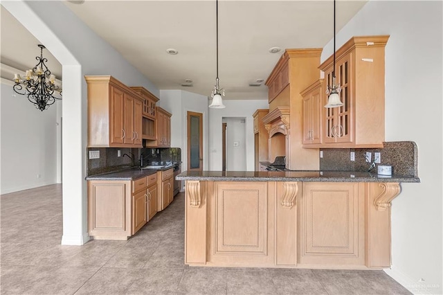 kitchen featuring decorative light fixtures, tasteful backsplash, dark stone counters, a peninsula, and glass insert cabinets