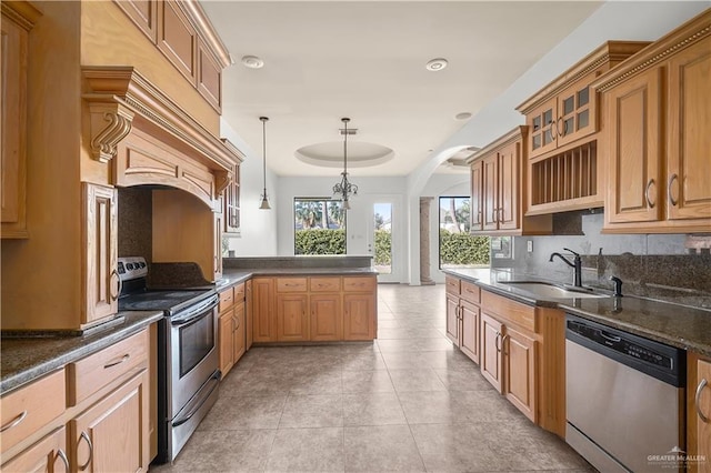 kitchen with a sink, appliances with stainless steel finishes, a peninsula, light tile patterned floors, and glass insert cabinets