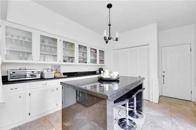 kitchen with dark stone counters, white cabinetry, hanging light fixtures, and a notable chandelier