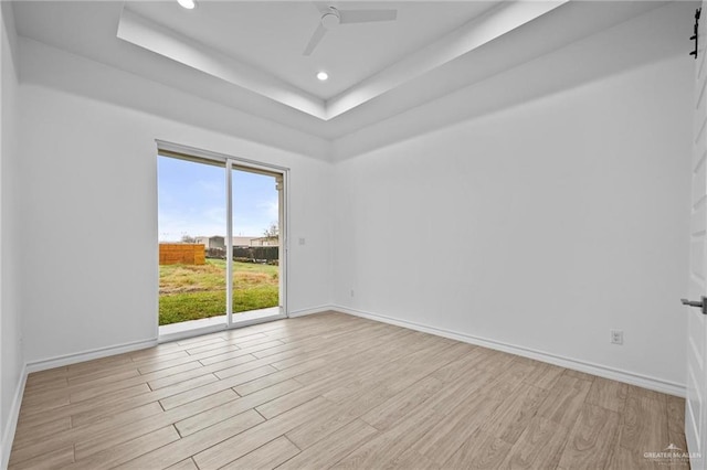 empty room with baseboards, a tray ceiling, wood finished floors, and recessed lighting