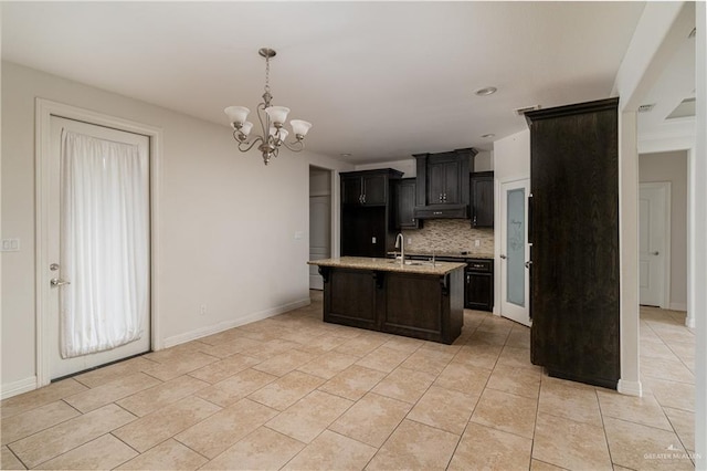 kitchen featuring backsplash, light tile patterned floors, an island with sink, decorative light fixtures, and a chandelier