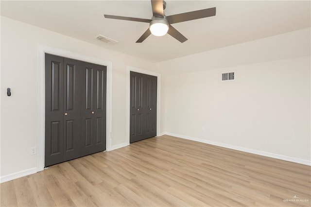 unfurnished bedroom with ceiling fan, lofted ceiling, two closets, and light wood-type flooring