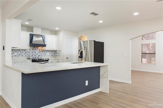 kitchen featuring white cabinetry, decorative backsplash, light hardwood / wood-style floors, stainless steel appliances, and wall chimney range hood