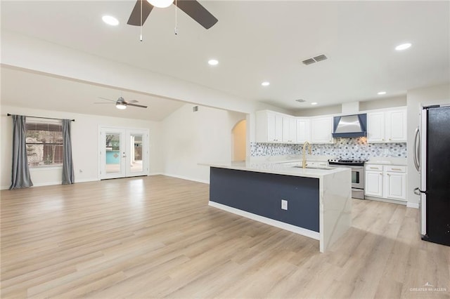 kitchen featuring appliances with stainless steel finishes, white cabinets, backsplash, light hardwood / wood-style floors, and wall chimney exhaust hood