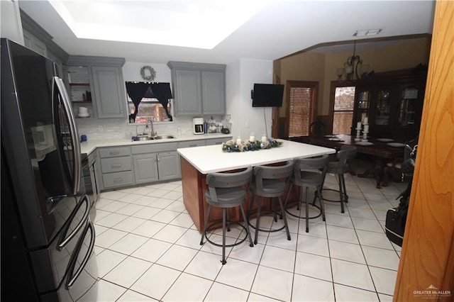 kitchen with gray cabinetry, a kitchen breakfast bar, stainless steel refrigerator, a kitchen island, and sink