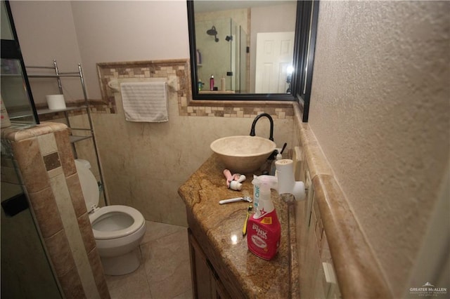 bathroom featuring toilet, a shower with door, tile patterned flooring, tile walls, and vanity