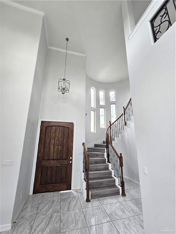 entrance foyer featuring marble finish floor, a notable chandelier, crown molding, baseboards, and stairs