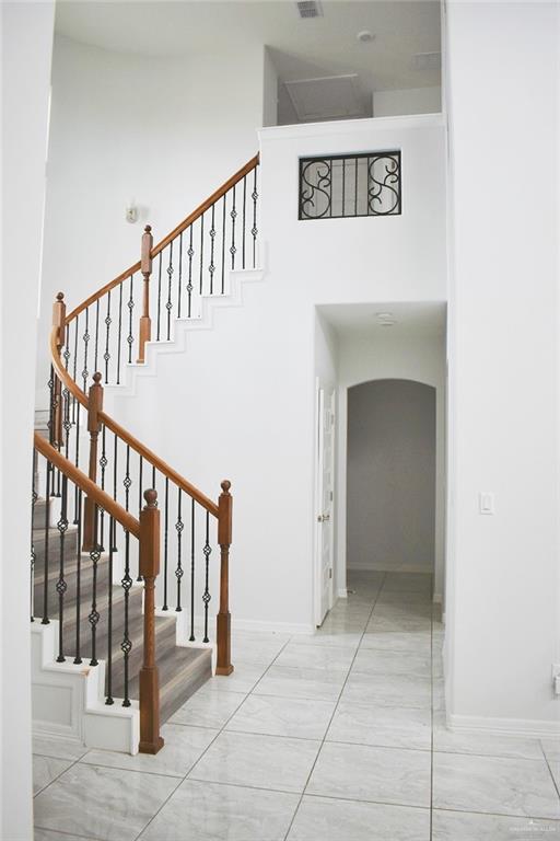 staircase featuring a towering ceiling, marble finish floor, baseboards, and arched walkways