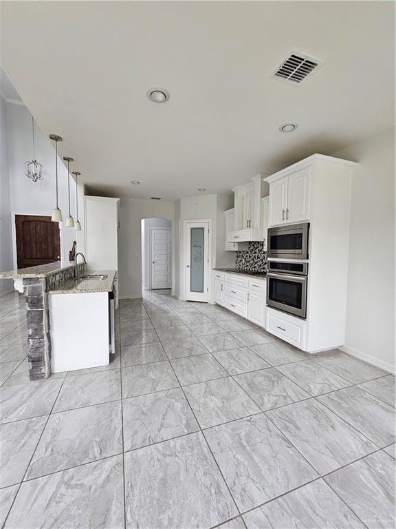 kitchen with a sink, visible vents, white cabinetry, appliances with stainless steel finishes, and backsplash