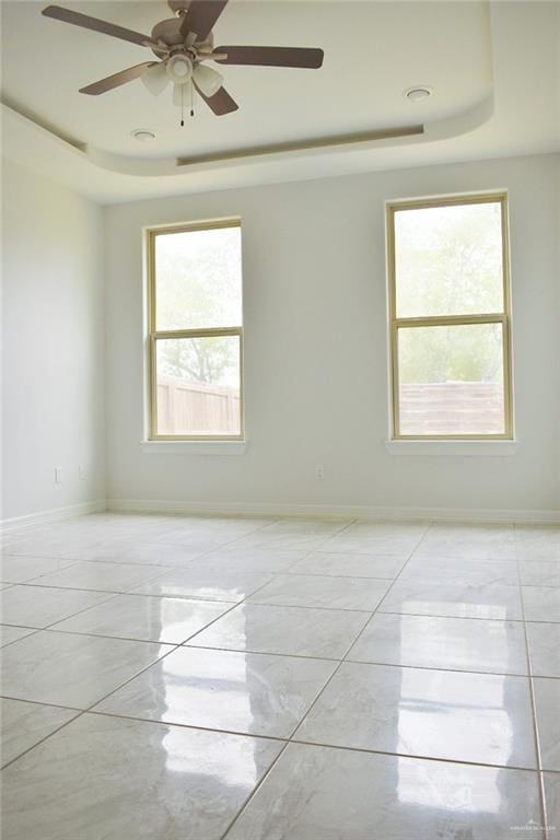 spare room featuring ceiling fan, a tray ceiling, and baseboards