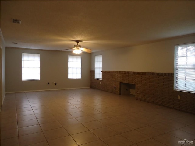 tiled empty room featuring ceiling fan and brick wall