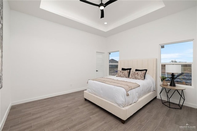 bedroom featuring a tray ceiling, baseboards, and wood finished floors