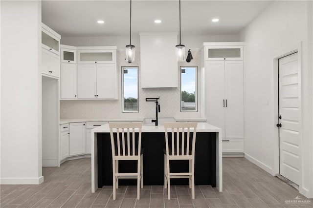 kitchen with light countertops, tasteful backsplash, a center island with sink, and white cabinetry