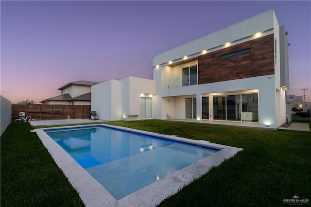 back house at dusk with a fenced in pool and a lawn