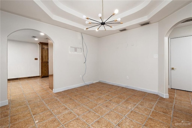 tiled spare room featuring a tray ceiling and a notable chandelier