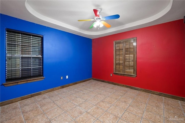 tiled empty room featuring ceiling fan and a raised ceiling