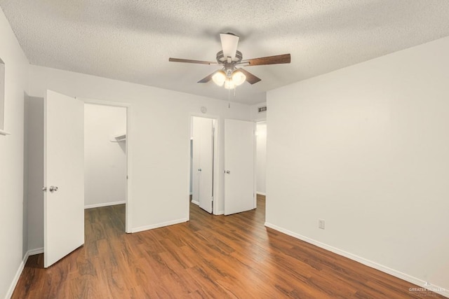 unfurnished bedroom featuring a walk in closet, ceiling fan, dark wood-type flooring, a textured ceiling, and a closet