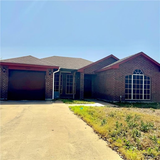 ranch-style home featuring a shingled roof, an attached garage, driveway, and brick siding