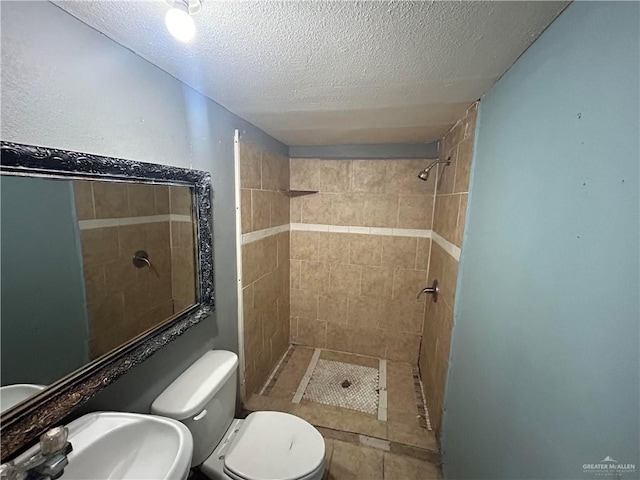 bathroom with a tile shower, sink, a textured ceiling, and toilet