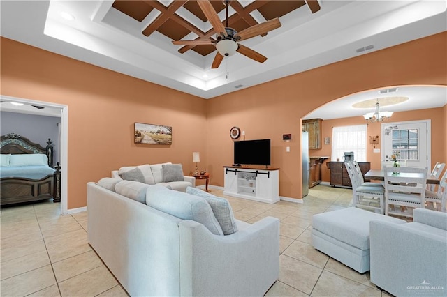 tiled living room with a raised ceiling and ceiling fan with notable chandelier