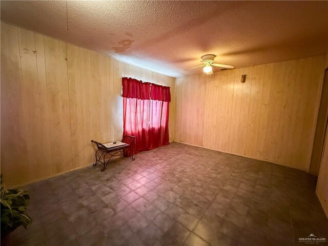 unfurnished room featuring a textured ceiling, ceiling fan, and wood walls