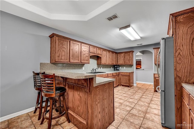 kitchen featuring kitchen peninsula, a kitchen breakfast bar, stainless steel fridge, sink, and backsplash