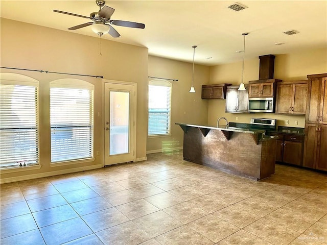 kitchen featuring hanging light fixtures, appliances with stainless steel finishes, light tile patterned floors, a kitchen island with sink, and a kitchen bar