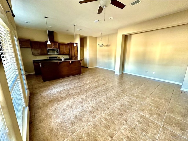 kitchen with decorative light fixtures, an island with sink, sink, ceiling fan, and a breakfast bar