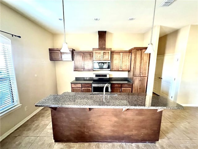 kitchen featuring appliances with stainless steel finishes, a kitchen bar, dark stone countertops, hanging light fixtures, and light tile patterned floors